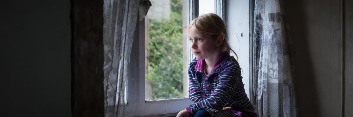 Young girl looking out of window in dark room