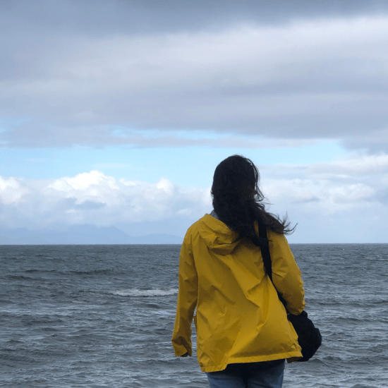 a lady in a yellow raincoat with hair blowing in the wind looking out to sea