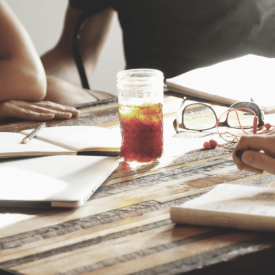 A table with notebooks and drinks as people are in discussion