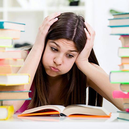 Student surrounded by books, looking confused