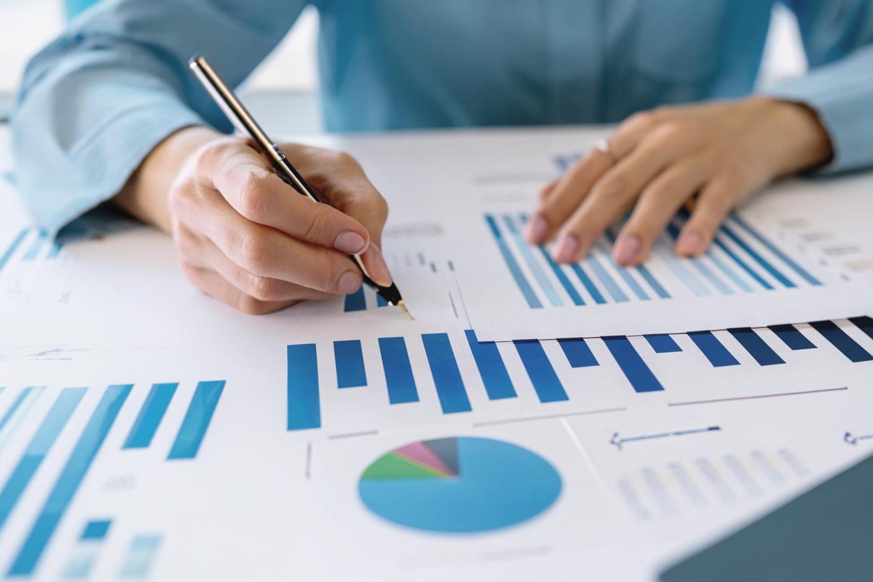 Woman writing ballpoint pen in documents with graphs