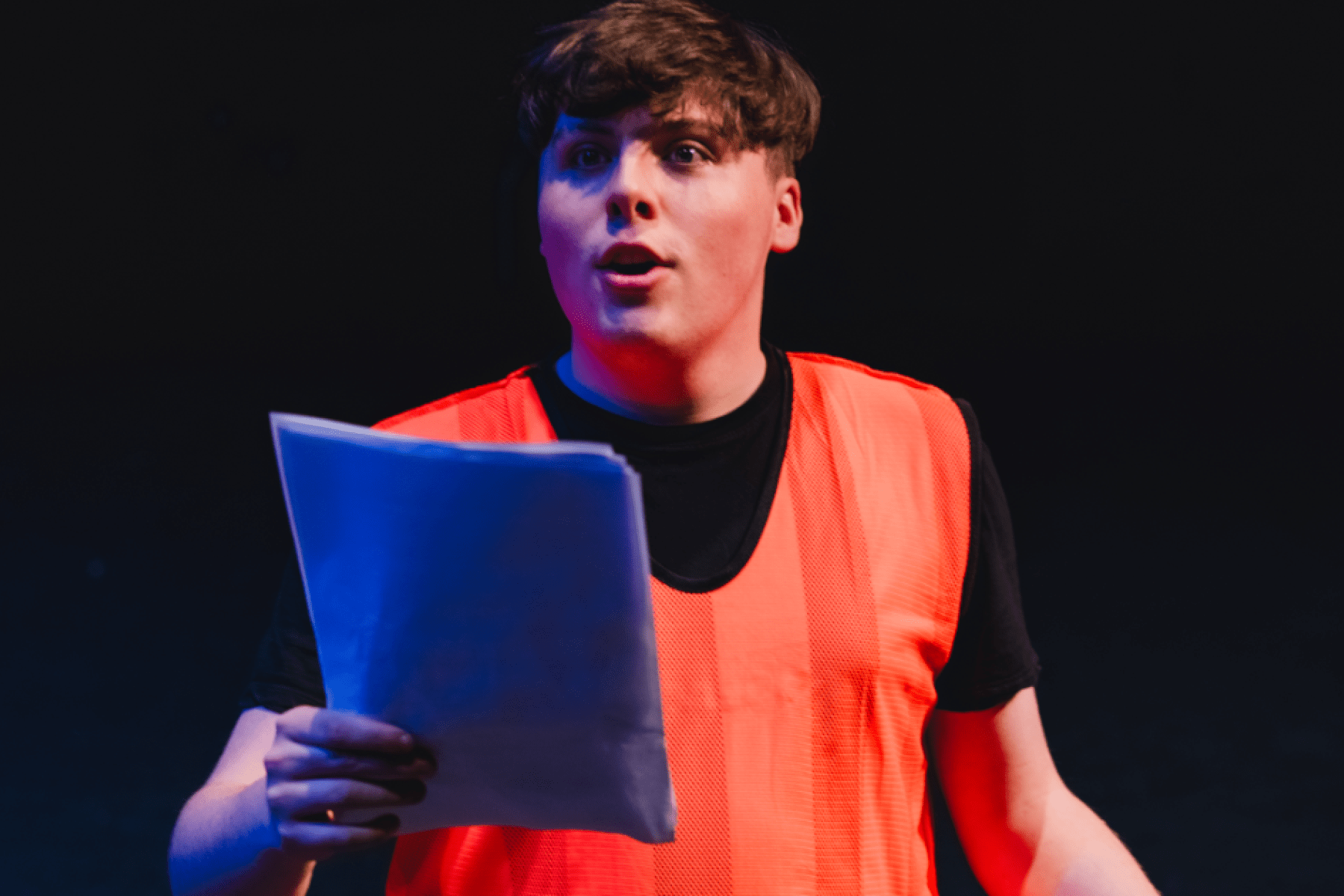 a man in a luminous orange vest reading from a script 