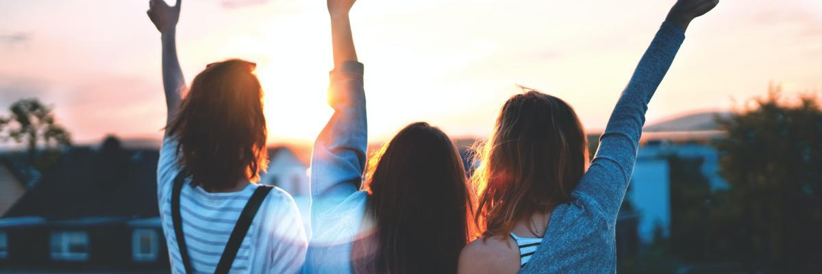 Three teenage girls waving to unseen person at sunset