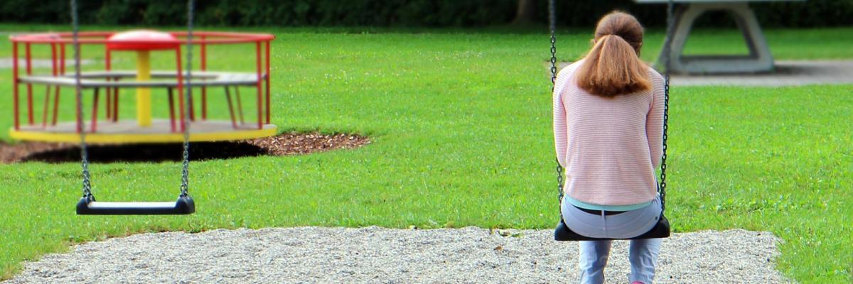 Girl alone on swing in play park looking sadly at the ground