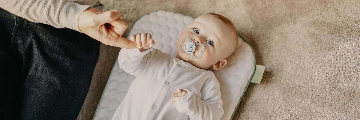 Infant with comforter holding a caring adult's hand