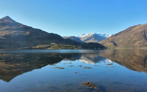 a snow capped mountain range being reflected in a lake a t the foot of the mountains