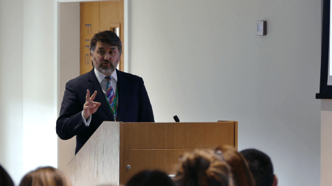 A man behind a lectern addressing an unseen audience