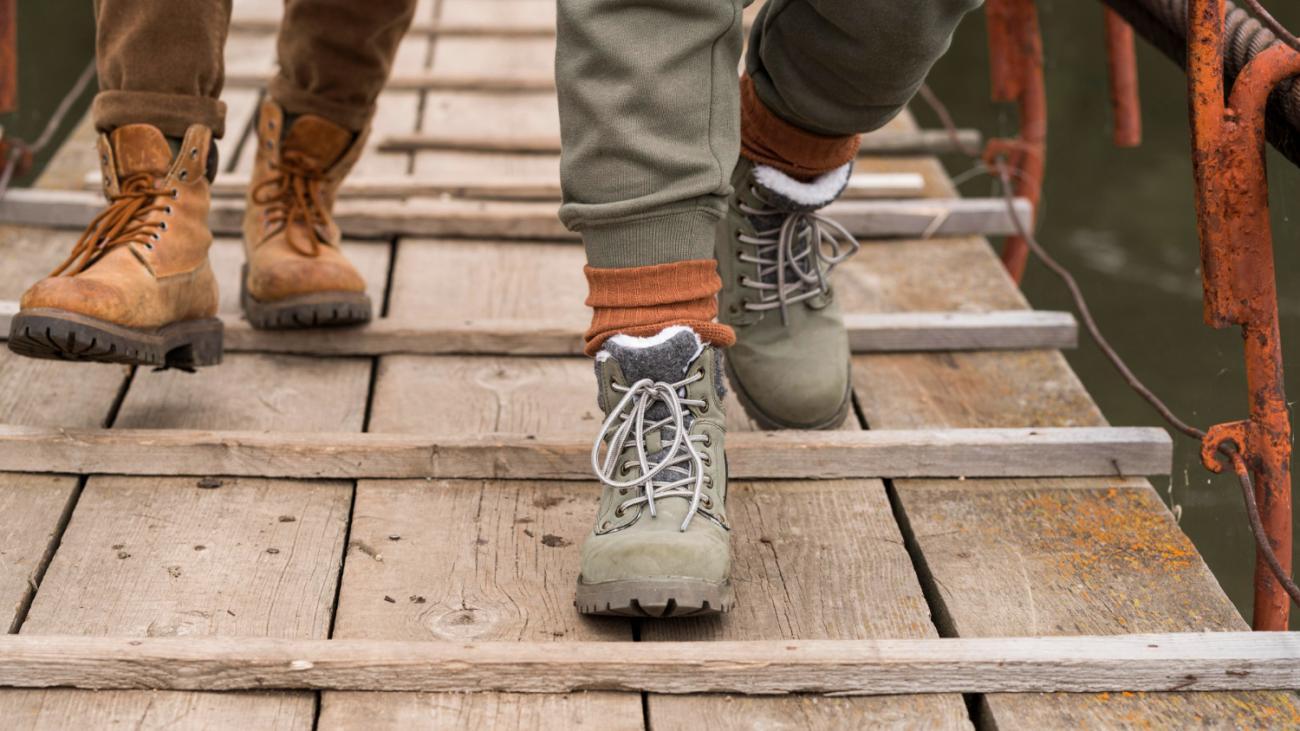 close up of two people's feet wearing hiking boots walking across a bridge