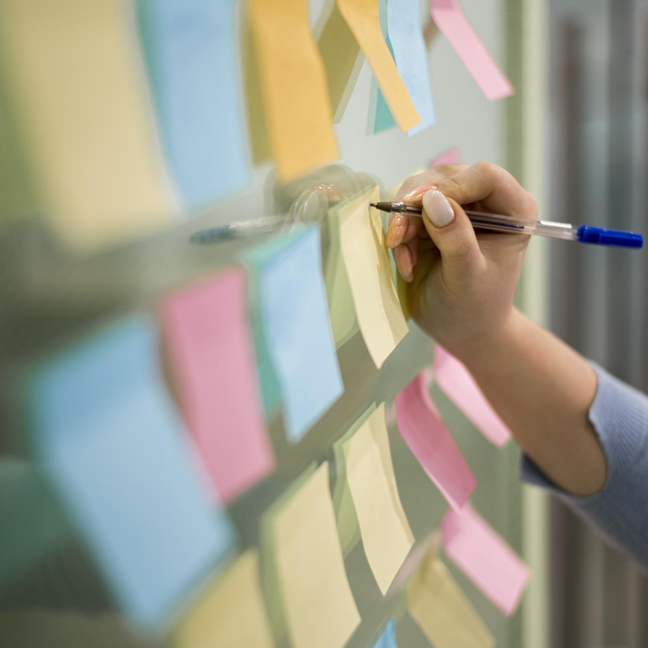 close up of many post it notes stuck on a wall with a person writing on one of them with a pen