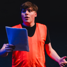 a man in a luminous orange vest reading from a script 