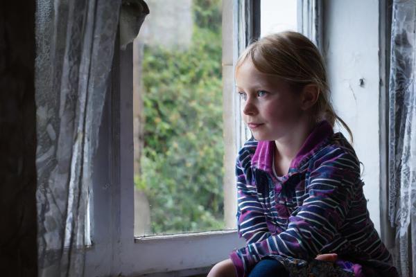 Young girl looking out of window in dark room