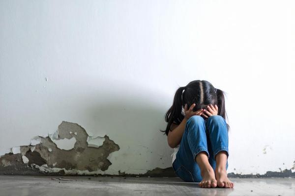 Child with head in hands seated on cold floor