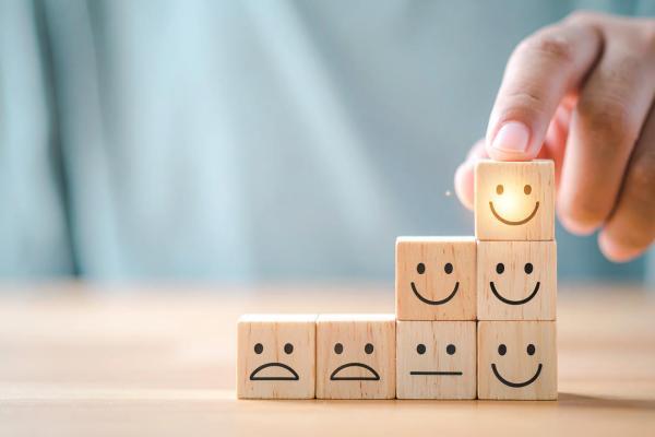 Stack of wooden blocks with faces on, with a finger pointing to a happy one